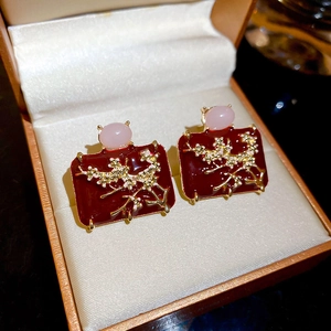 Detail view of red enamel earrings with golden plum blossom and pink stone