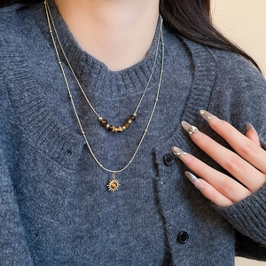 Detail of layered gold necklace with sun pendant and tiger eye beads on model