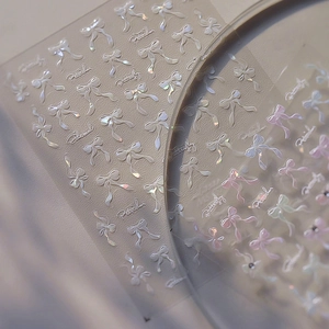 Macro detail of holographic bow nail stickers with ethereal art typography accents