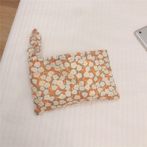Detailed top view of orange floral cotton pouch with matching handle strap on quilted fabric