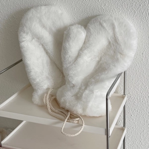 Detail shot of plush white faux fur mittens with a thick woven lanyard on a shelf