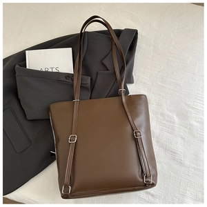 Deep brown faux leather tote bag with adjustable straps on a white textured background