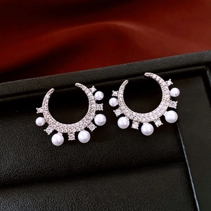 Macro detail of silver C-shaped earrings with cubic zirconia and small white pearls