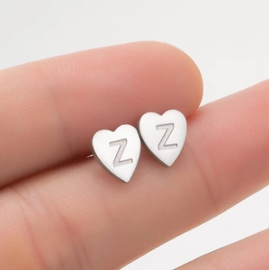 Gros plan d'une boucle d'oreille cœur argentée avec gravure Z tenue par les doigts