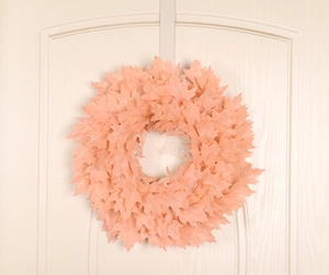 Pink and orange maple leaf Christmas wreath hanging on a beige door for home decor