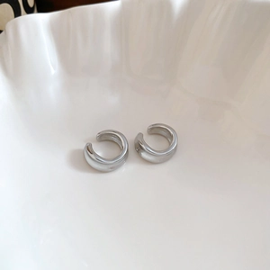 Silver geometric C-shaped ear cuffs displayed in a white porcelain shell dish