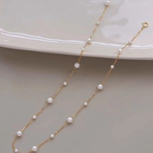 Detail of gold chain necklace featuring staggered white pearls and a secure round clasp