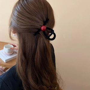 Detail of a velvet hair claw clip with red bead accent worn by a model in a cozy setting