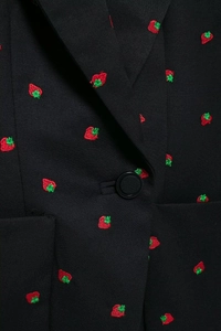 Vue détaillée de broderies fraises rouges sur le tissu d'un blazer noir à boutons