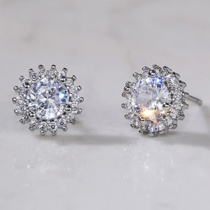 Macro shot of a silver sunflower zircon earring on a light marble surface with reflections