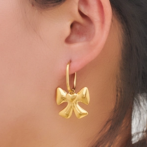 Detail shot of a golden bow earring with heart motif worn by a model in soft lighting