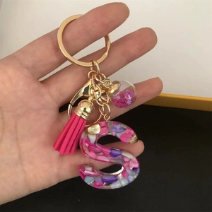 Detail of resin letter S keychain with pink glitter ball and soft tassel accent