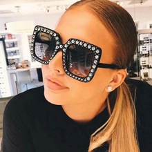 Close-up of oversized square black sunglasses featuring sparkling silver rhinestones