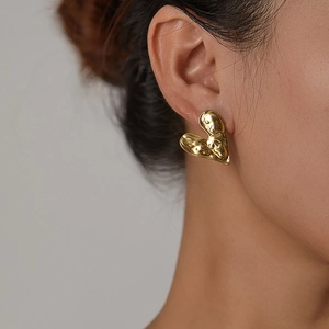 Close-up of golden irregular heart earring with textured lava finish on model's ear