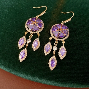 Detail of vintage gold tassel earrings with purple zircon clusters on green velvet
