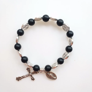 Macro shot of St. Benedict medals and cross charms on matte black lava stone bead bracelet