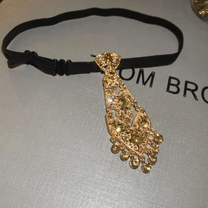 Macro detail of gold tie-shaped pendant with amber rhinestones and tassel charms
