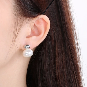 Close-up of a silver stud earring featuring a white baroque pearl on a female model