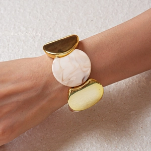 Dettaglio del bracciale elastico in metallo dorato e acrilico con trama marmorea al polso