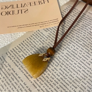 Macro detail of a fan-shaped yellow stone pendant with leather cord and wooden bead