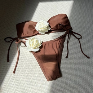 Flat lay of brown bikini set featuring 3D white rose details and side tie bottoms