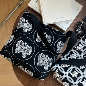 Detailed close-up of butterfly embroidery on vintage black canvas tote bag with wooden background