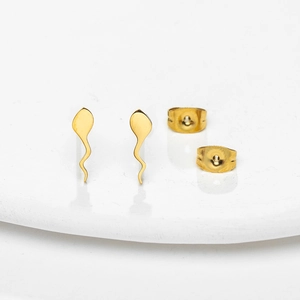 Macro detail of gold tadpole-shaped stud earrings with butterfly backings on a white tray