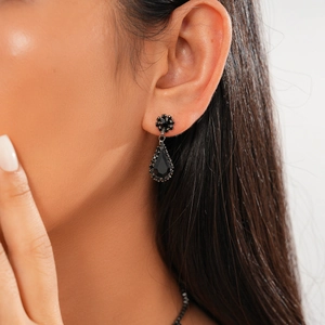 Close-up of black teardrop earrings with gothic floral design on a female model