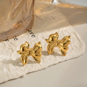 Elegant gold bow earrings with polished mirror finish on textured paper background