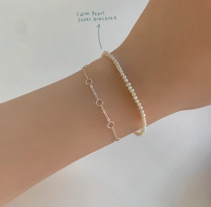 Close-up of minimalist layered S925 sterling silver chain and delicate pearl bracelet