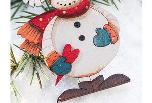 Detail of wooden snowman ornament with red scarf on snowy background and pine needles