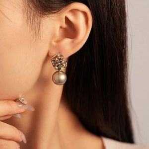 Macro view of vintage gold earrings featuring rhinestones and a grey pearl on ear