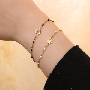 Close-up of golden sun pendant bracelets with black and white beads on a wrist