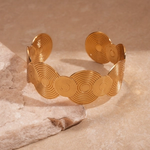Close-up of golden cuff bracelet with concentric circular texture on natural stone