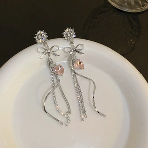 Macro detail of long silver bow earrings with pink heart crystals on a white tray