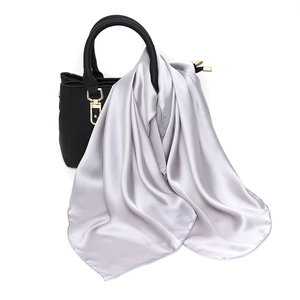 Silver satin square scarf tied on a black handbag showing elegant drape and silk texture