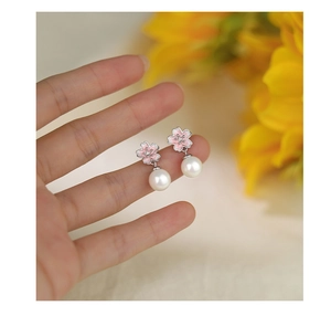 Close-up of handmade pink cherry blossom earrings with white pearls held in hand