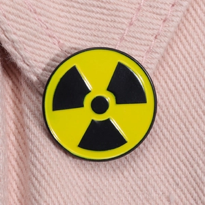 Close-up of yellow radiation symbol enamel pin on pink denim fabric showing metal texture
