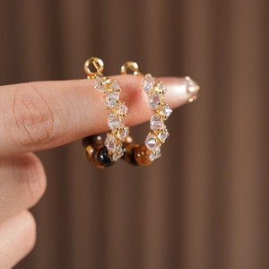 Close-up of gold hoop earrings featuring tiger eye beads and zircon crystals on fingers