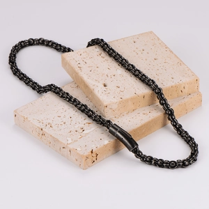 Minimalist black stainless steel pearl necklace on textured beige stone blocks