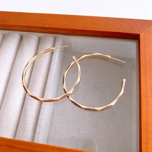 Detailed macro view of golden hoop earrings with geometric diamond-cut textures in a box