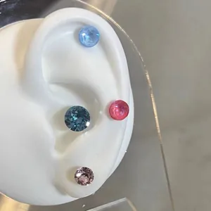 Detailed macro view of four colorful round zircon stud earrings on a white silicone ear model