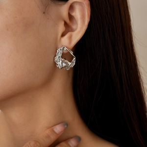 Detail of silver irregular crumpled metal earrings worn by a model on beige background