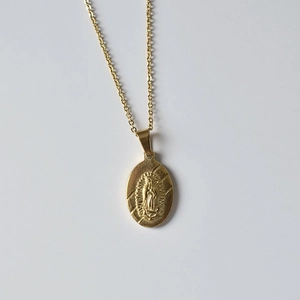 Détail d'un collier pendentif ovale doré avec relief de la Vierge Marie sur fond blanc