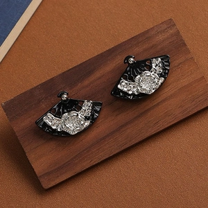 Macro detail of vintage black fan-shaped earrings with floral patterns on a wood base