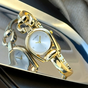 Detail of gold women's watch with horseshoe case and crystal markers on silver tray