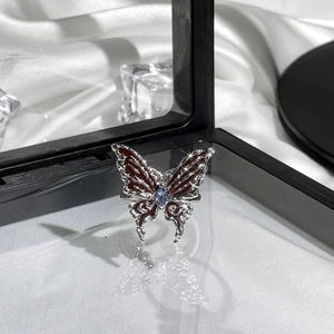 Macro shot of silver butterfly ring with red enamel and blue gemstone on white satin