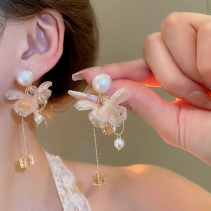 Dettaglio di orecchini a fiore con nappe, perle e petali traslucidi sul modello