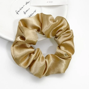 Elegant champagne gold satin scrunchie displayed on a minimalist white ceramic plate