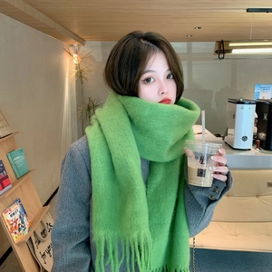 Close-up of a green mohair scarf with fringe detail worn in a cozy cafe setting